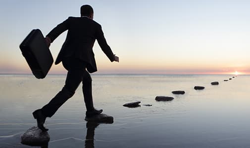 business man stepping from stone to stone across a body of water