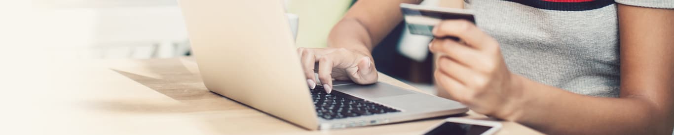 Young woman holding a credit card and typing on a laptop.