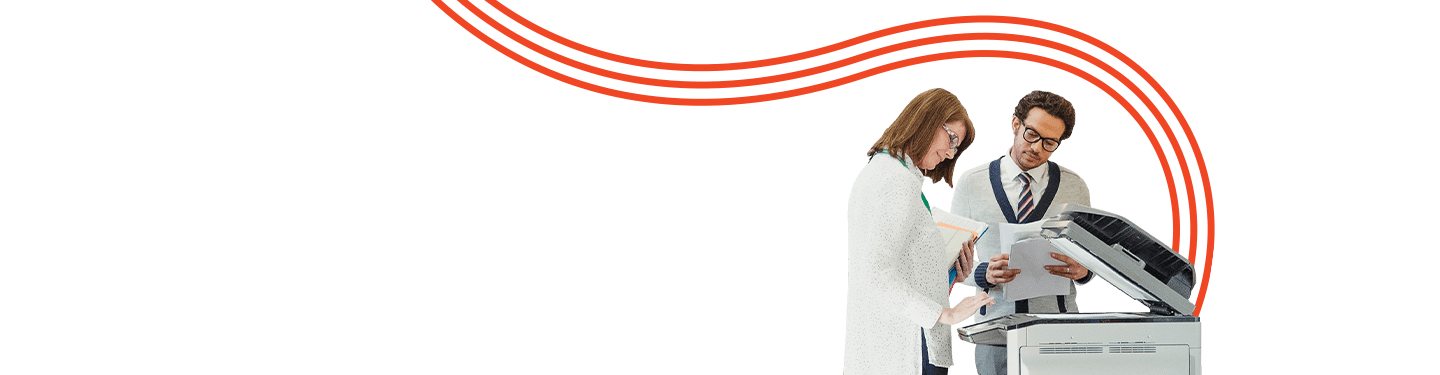 Two educators review documents next to a photocopier in a school hallway, illustrating efficient printing solutions for K-12 budgets.