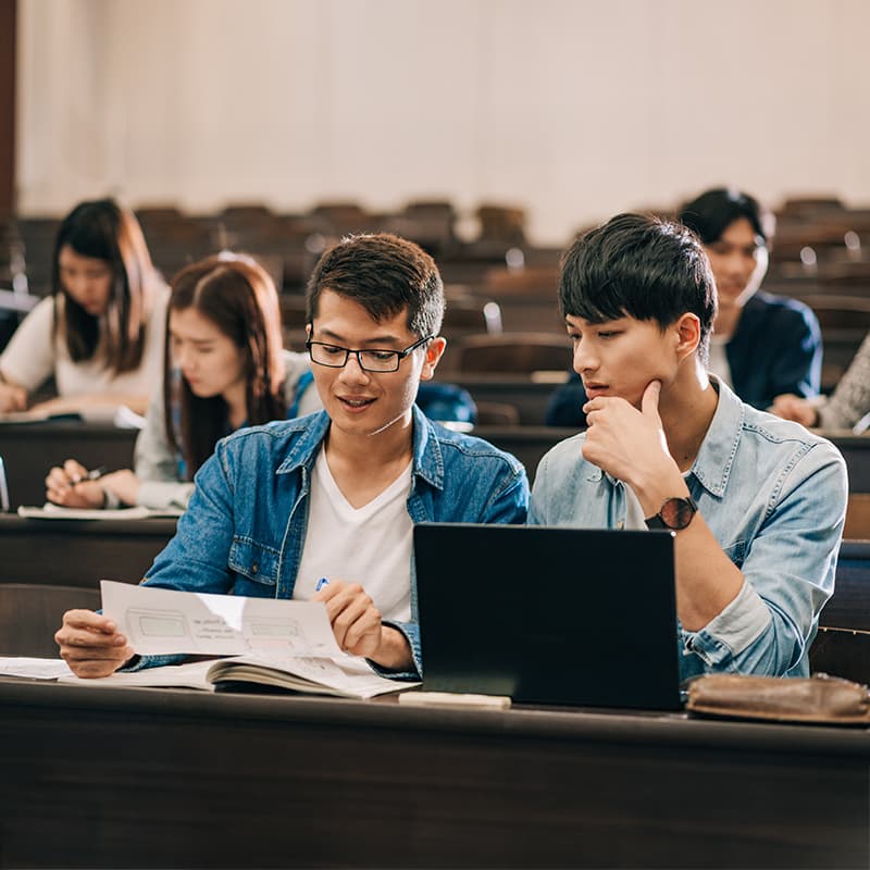 Happy college students reviewing a paper document and using a laptop, demonstrating Ricoh Scholars Program