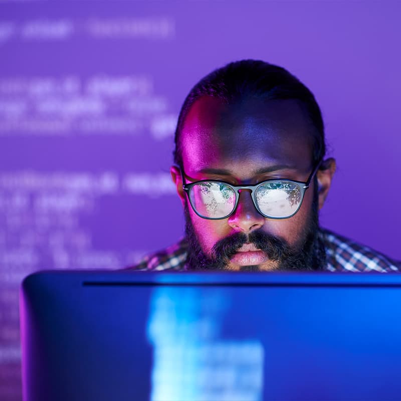 Man working on a desktop with illegible code projected on the wall behind him