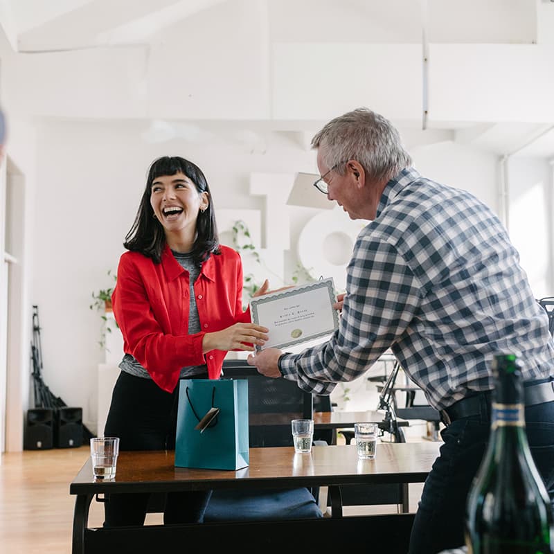 A happy woman receiving a certificate from an older man, demonstrating Ricoh's recognition programs and incentives