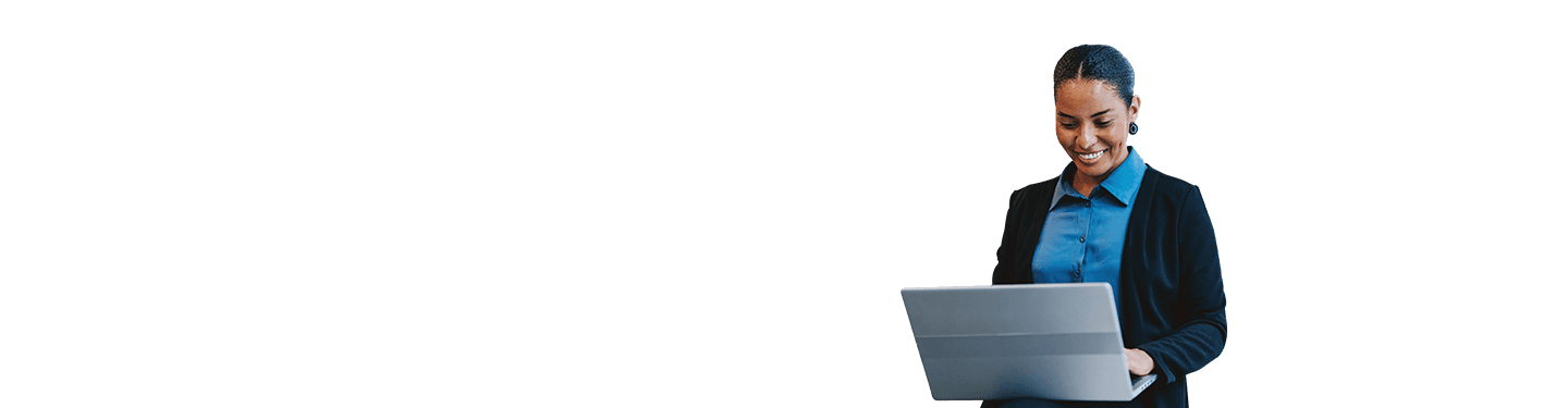 A confident woman smiling while using a laptop, standing near a large window, representing engagement with Microsoft 365 Business Premium.